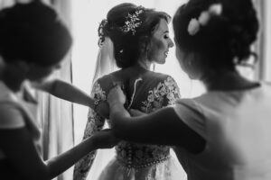 Bridesmaids helping happy bride fit in dress